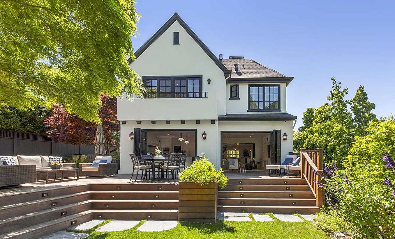 A beautifully remodeled two-story American Craftsman house featuring a gabled roof, large folding glass doors, and an outdoor deck with seating.