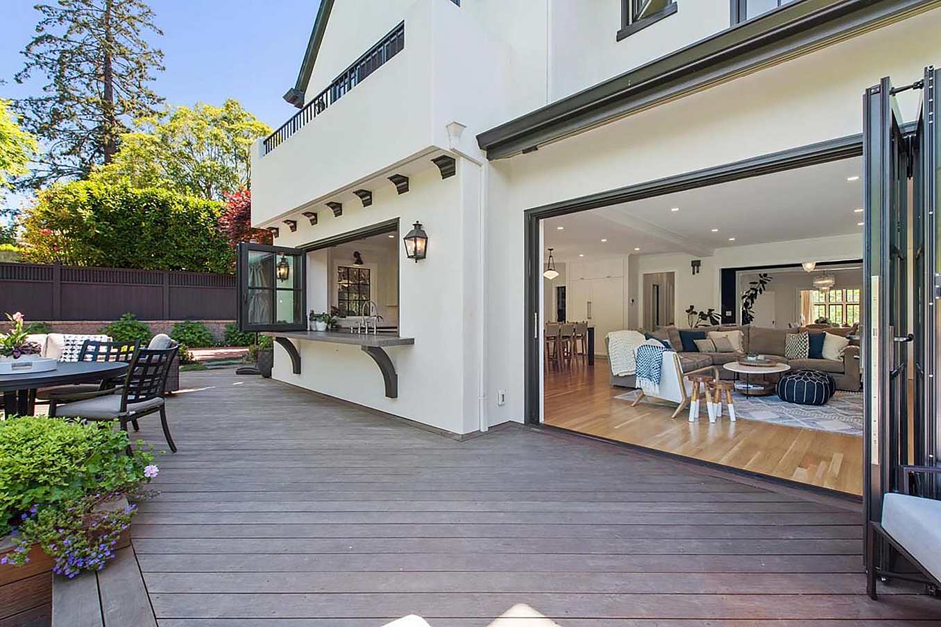 Spacious patio with wooden decking, outdoor seating, and large folding glass walls leading to a modern living room with light-colored furniture, perfectly blending style and functionality for any remodeling project.