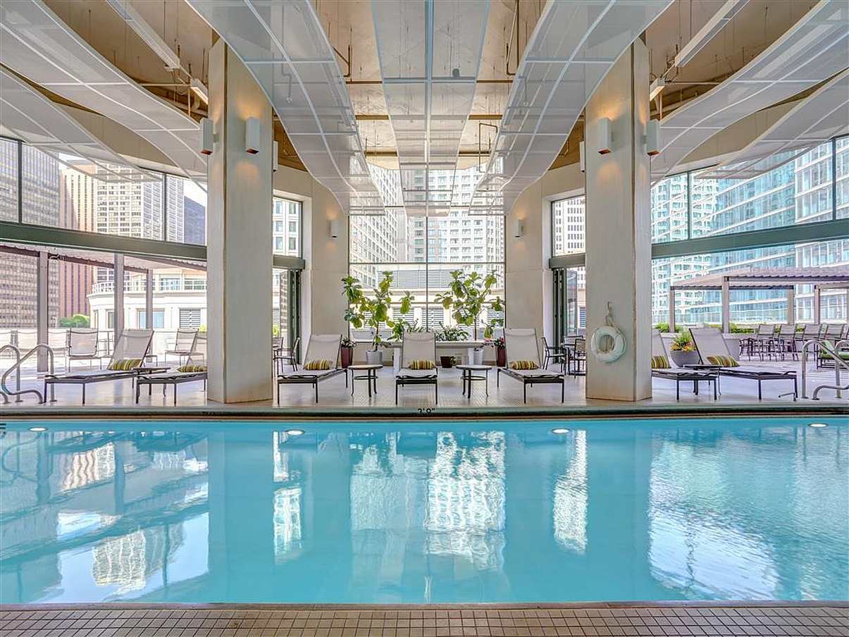 Indoor pool with lounge chairs, city views, and opening glass doors for fresh air and easy access.