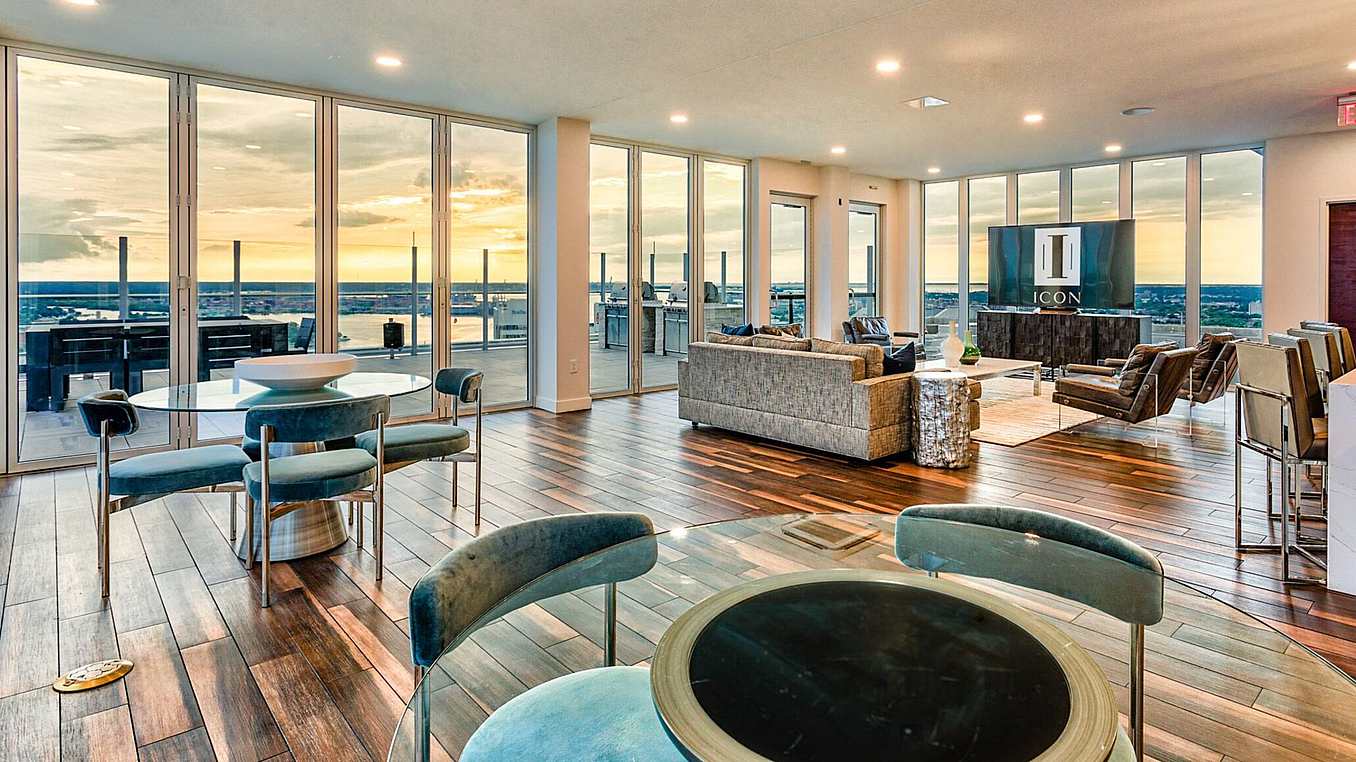 Modern commercial rooftop lounge with opening glass doors, wooden floors, and cityscape sunset views.