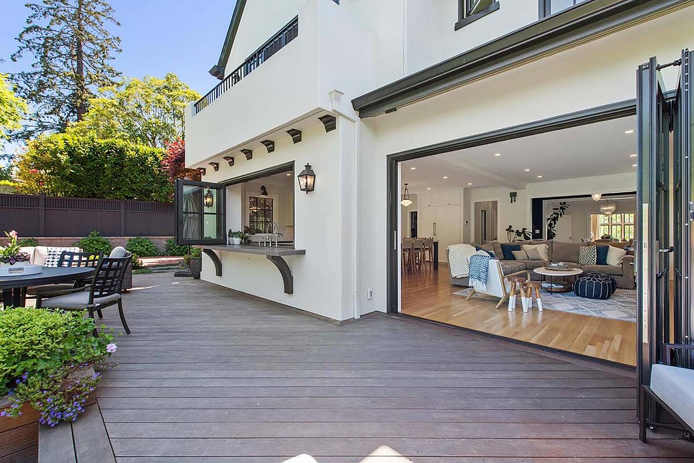 Spacious patio with wooden decking, outdoor seating, and large folding glass walls leading to a modern living room with light-colored furniture, perfectly blending style and functionality for any remodeling project.