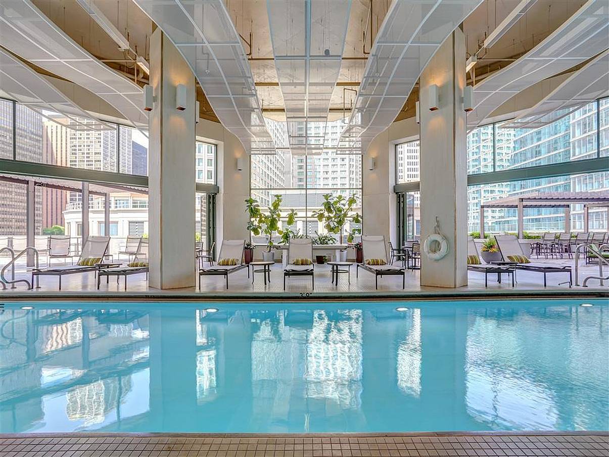 Indoor pool with lounge chairs, city views, and opening glass doors for fresh air and easy access.