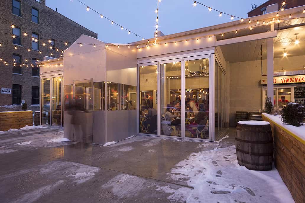Snowy outdoor restaurant patio with String Lights featuring commercial glass doors showing indoor dining.