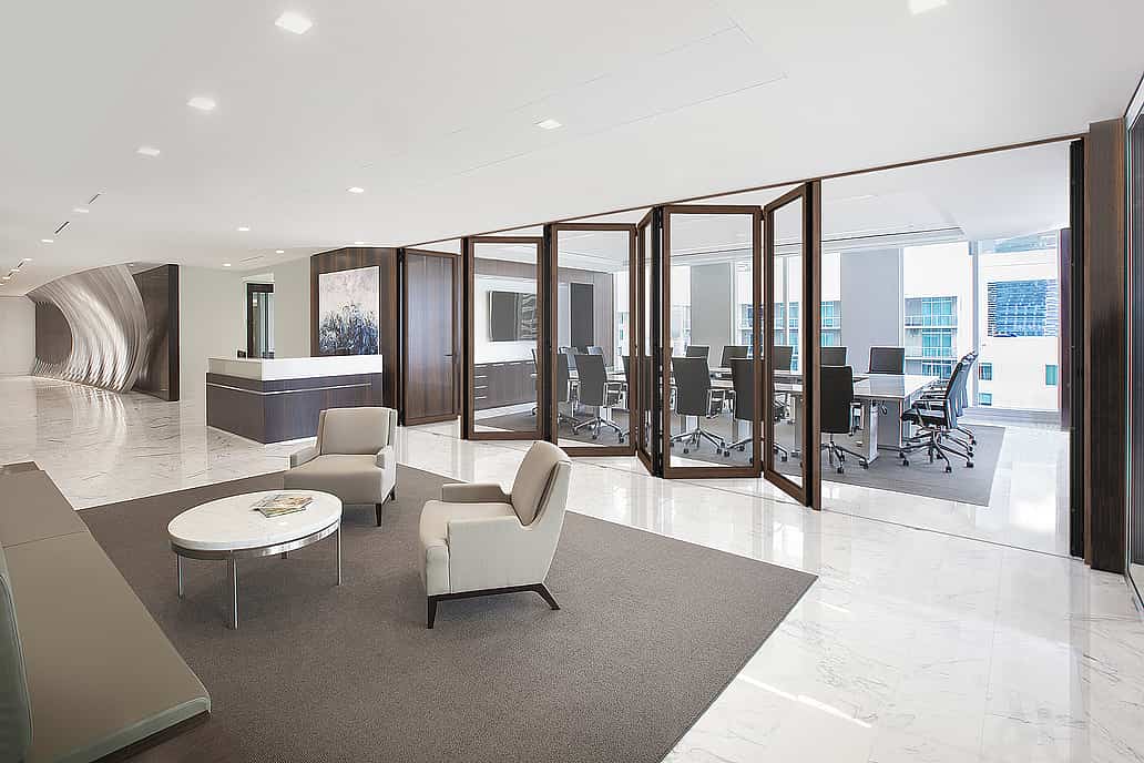 Modern office interior with a glass-partitioned conference room with a long table and chairs, enhanced by interior wood-framed folding glass doors for superior acoustical control.