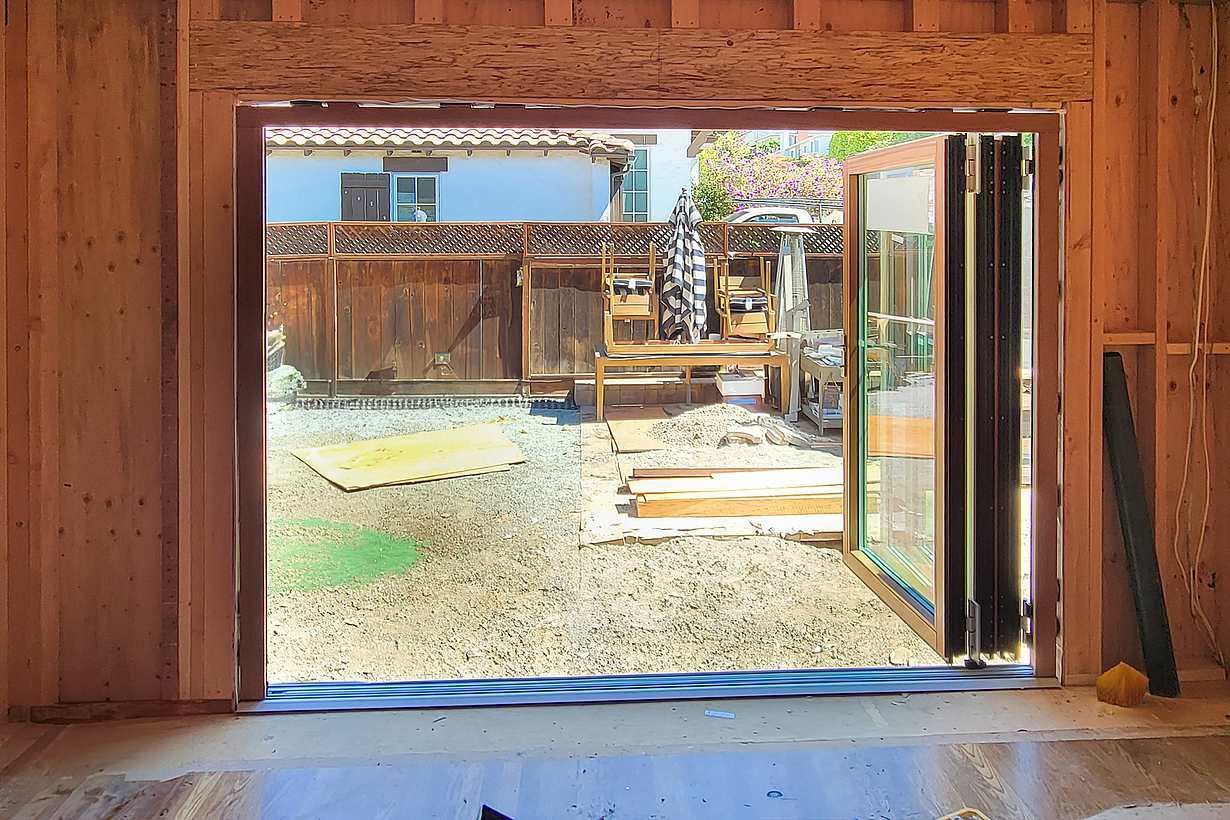 Partially constructed wooden frame of a room with large open folding glass doors leading to a backyard,