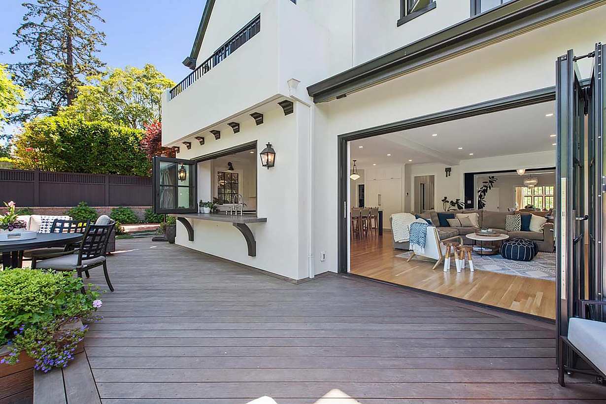 Spacious patio with wooden decking, outdoor seating, and large folding glass walls leading to a modern living room with light-colored furniture, perfectly blending style and functionality for any remodeling project.