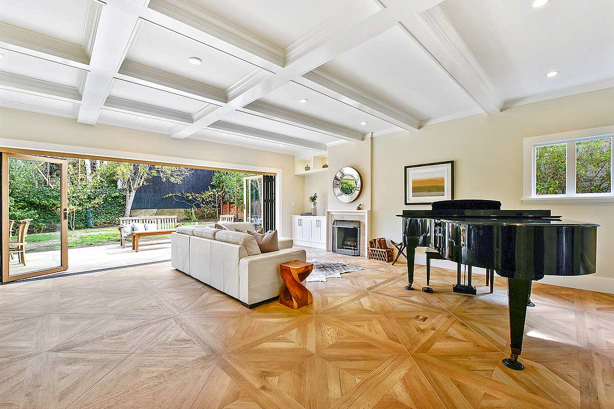 Spacious living room with large glass folding doors open to a patio and garden. Light wooden floor with a geometric pattern adds charm to the Craftsman house remodeling.