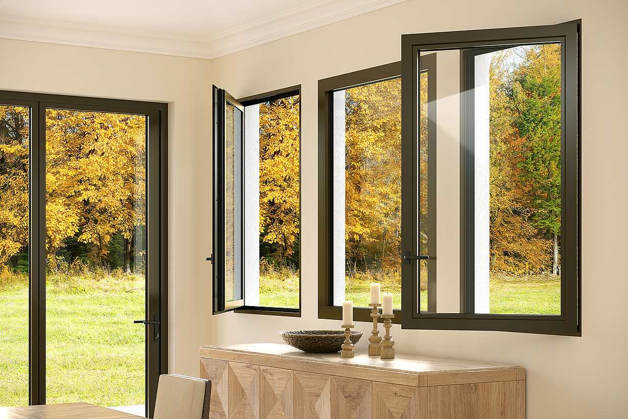 Dining room interior with three tilt-turn windows and a sliding glass door, revealing a view of trees with autumn foliage.
