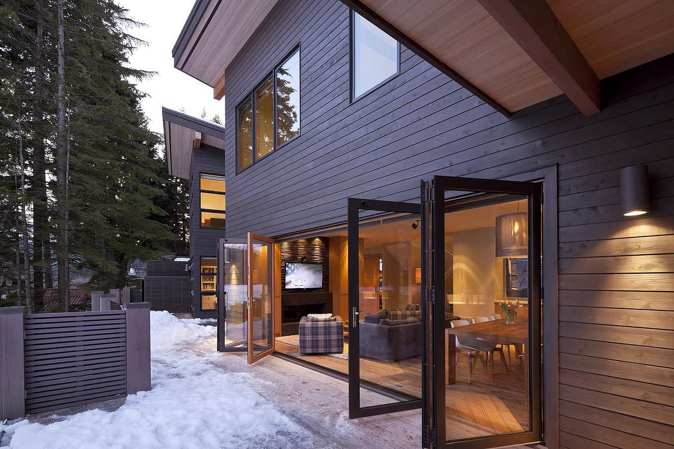 A house in the woods with a wooden deck and aluminum clad folding doors