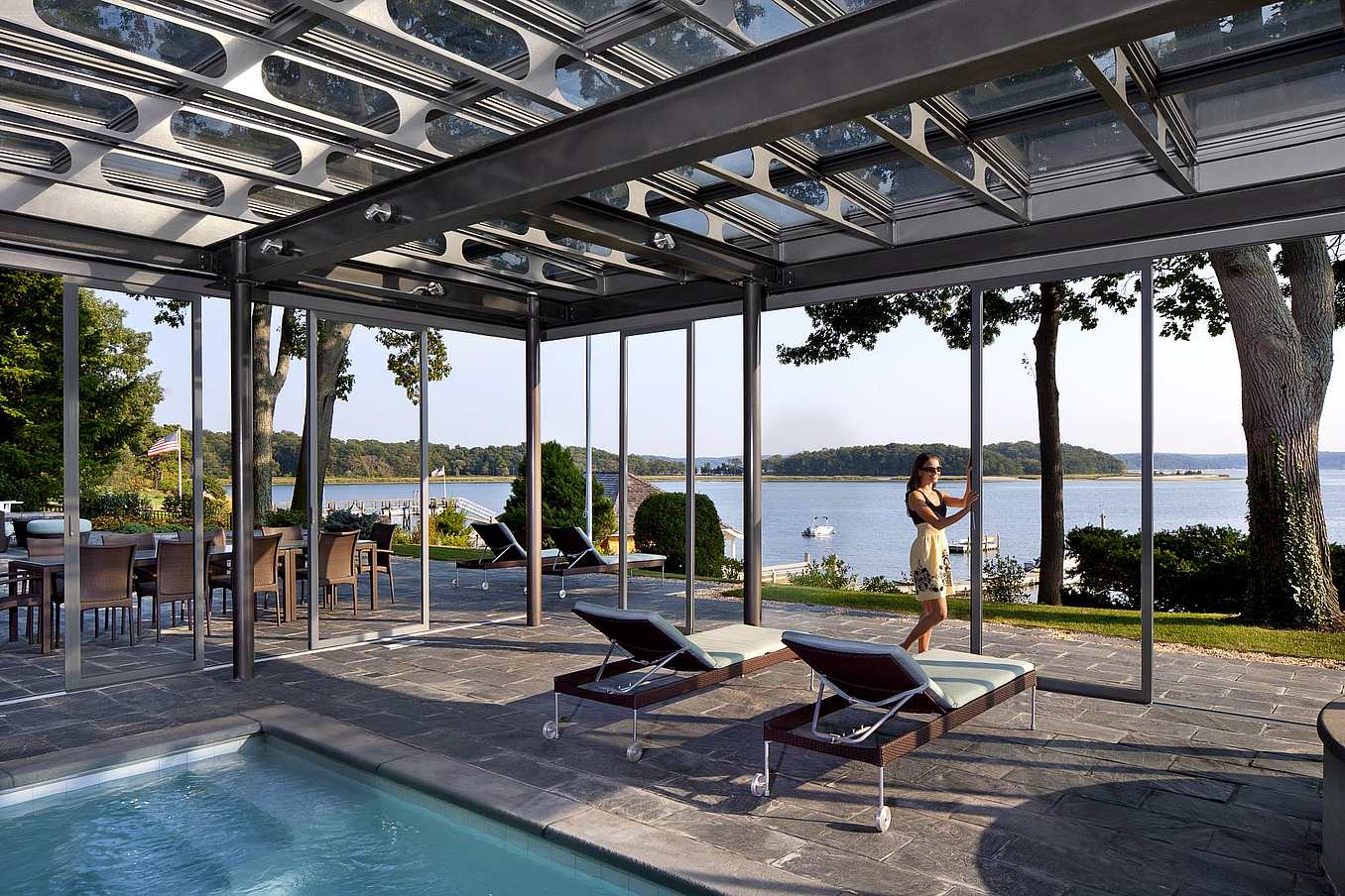 Modern outdoor patio with pool. A women is adjusting the sliding glass door, demonstrating how large openings are possible with unlimited spans of individual panels for an unobstructed view.