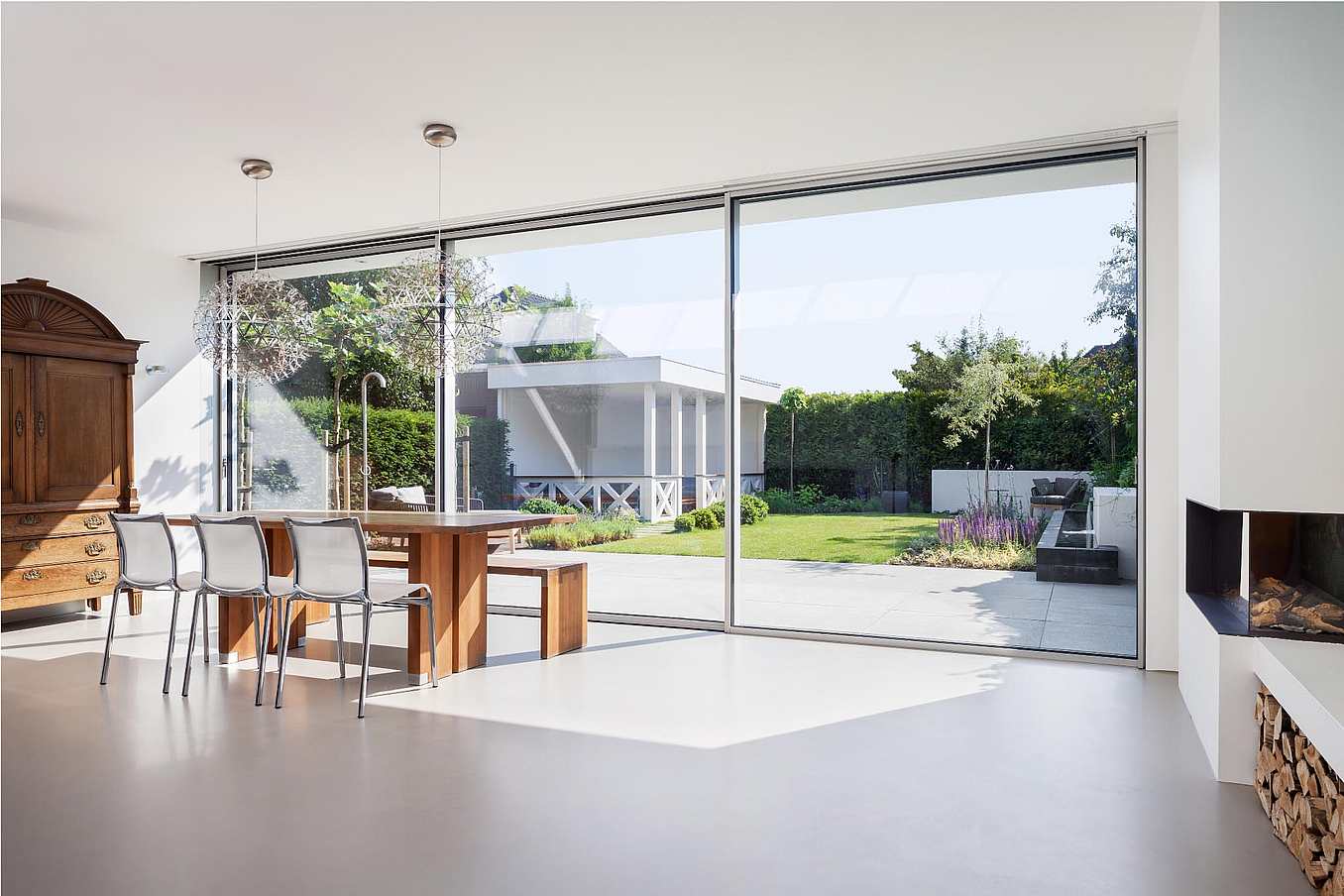 Modern dining area with sliding glass doors opening to a green backyard with patio and outdoor seating.