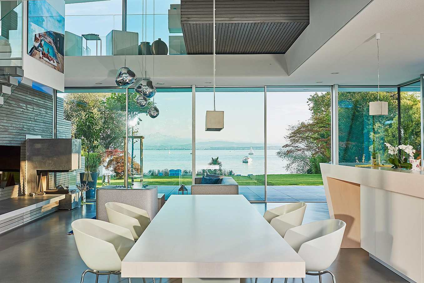 Modern open-plan living and dining area with sliding glass doors opening to scenic lake views with boats and lush trees.