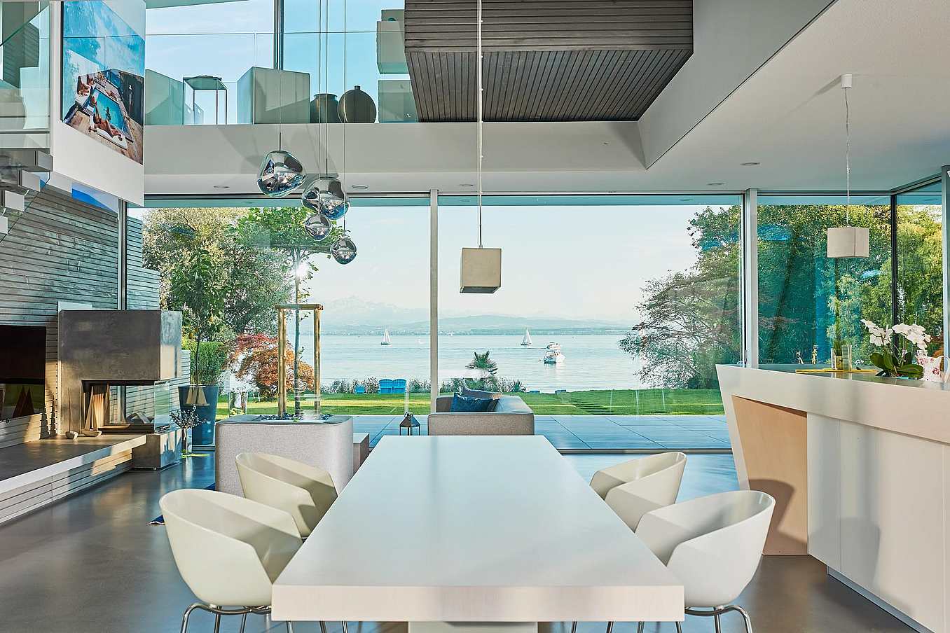Modern open-plan living and dining area with sliding glass doors, lake views with sailboats, and contemporary decor.