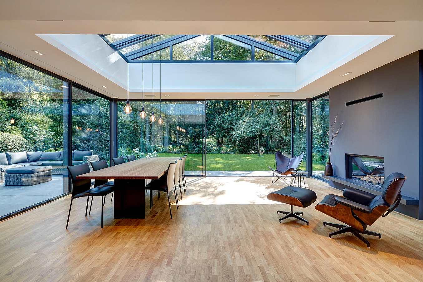 Modern open-plan living and dining area with sliding glass doors, skylight, wooden floors, garden views, and a fireplace.