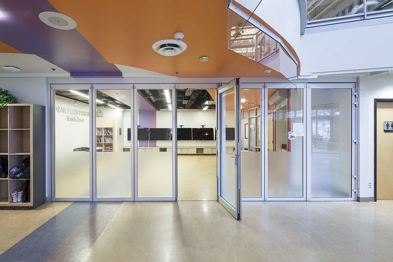 Kelowna YMCA youth zone featuring sliding glass doors, a swing door, frosted lower panels, and an open glass entryway.