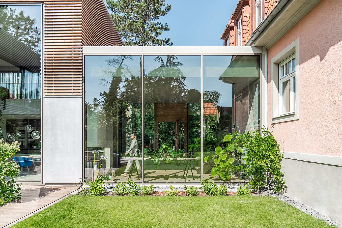 Modern living room exterior with sliding glass doors, lush greenery, and seamless indoor-outdoor flow.