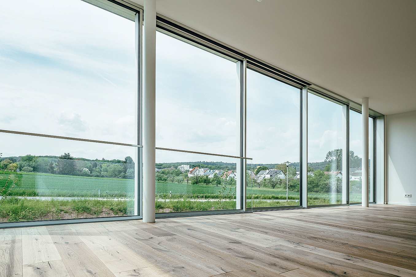 An empty room with large windows and wood floors showcasing minimal sliding glass walls