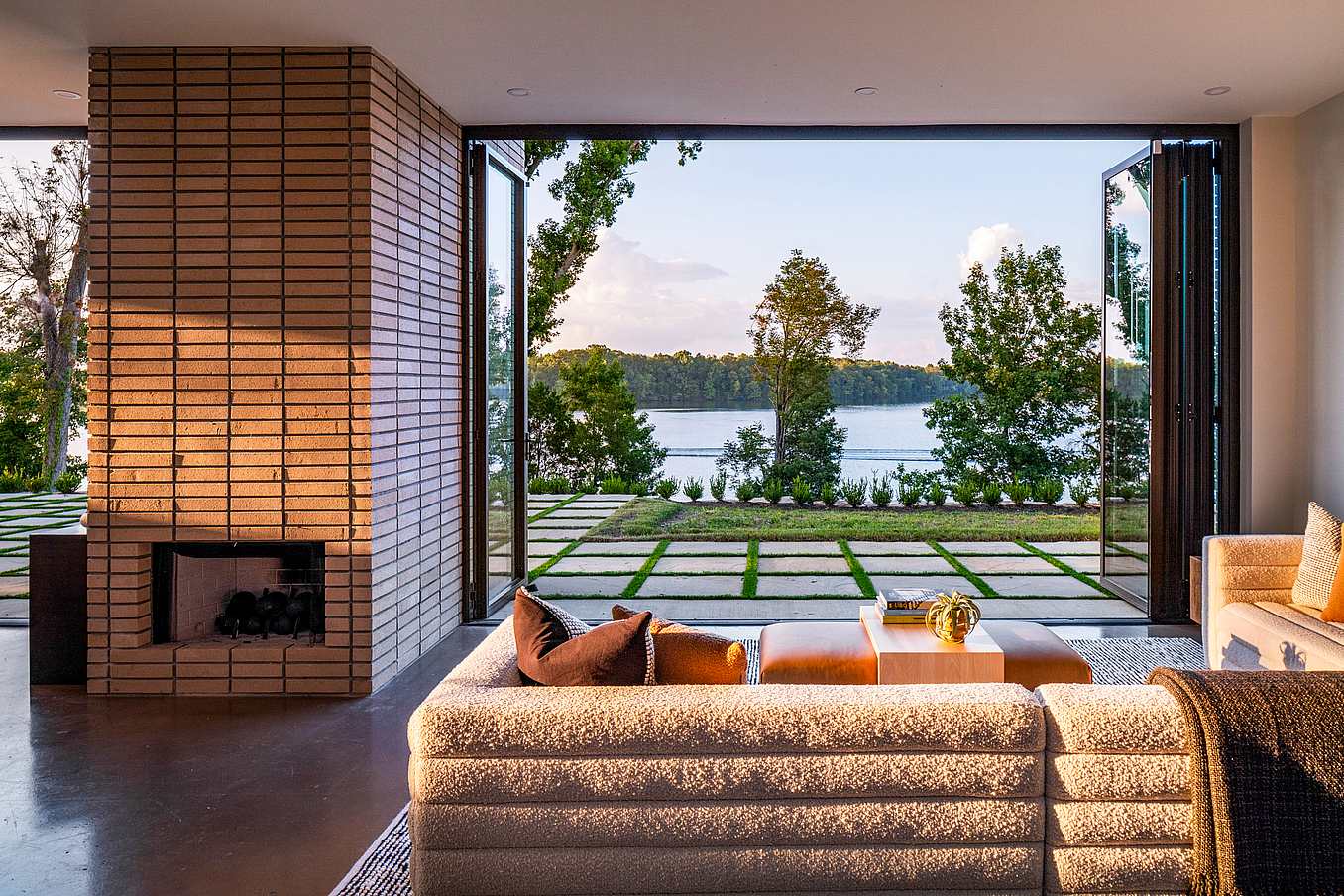 A modern living room with folding patio doors reveals a view of a lake. 