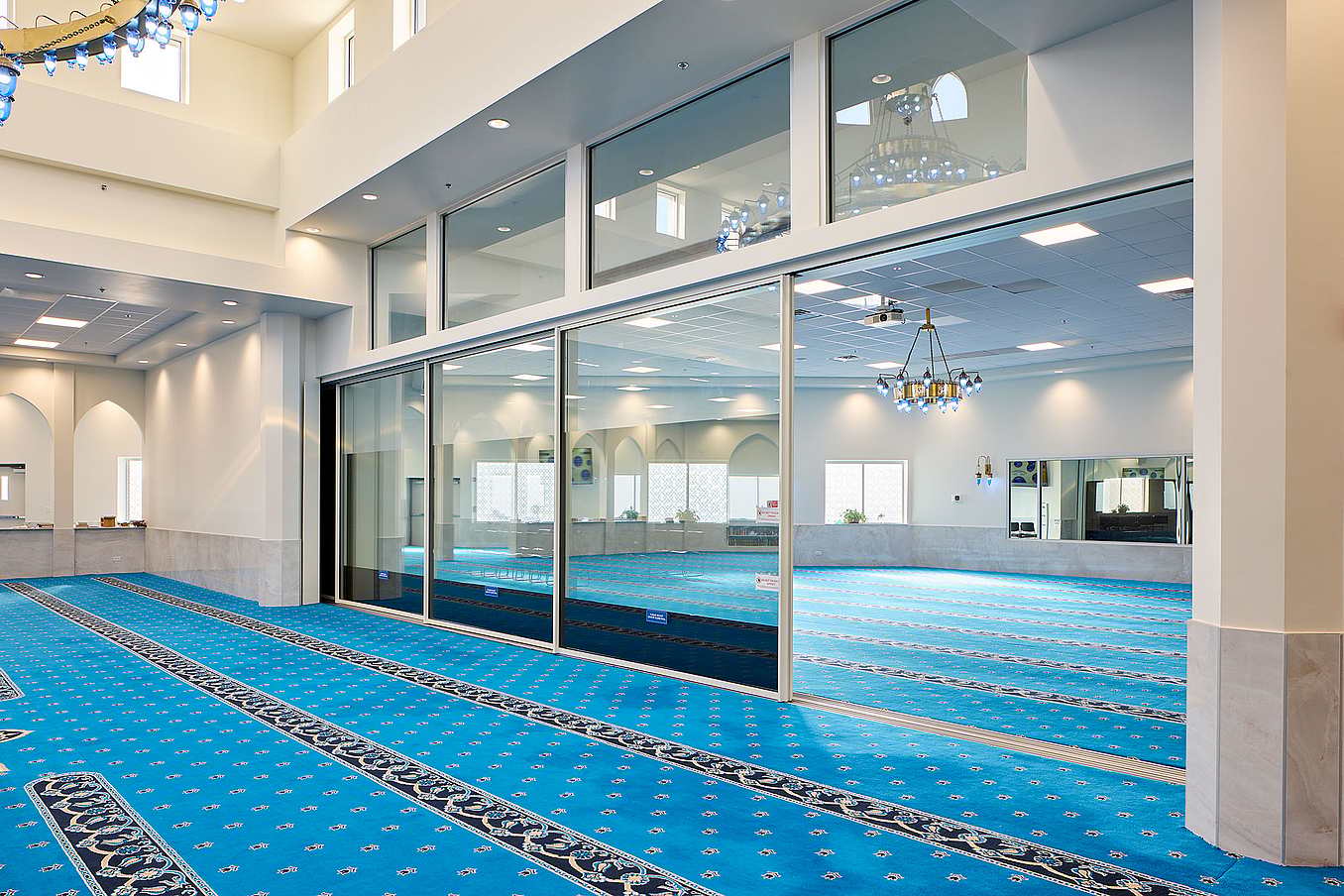 The interior of the mosque features large sliding glass doors with transoms that open up to invite natural light.