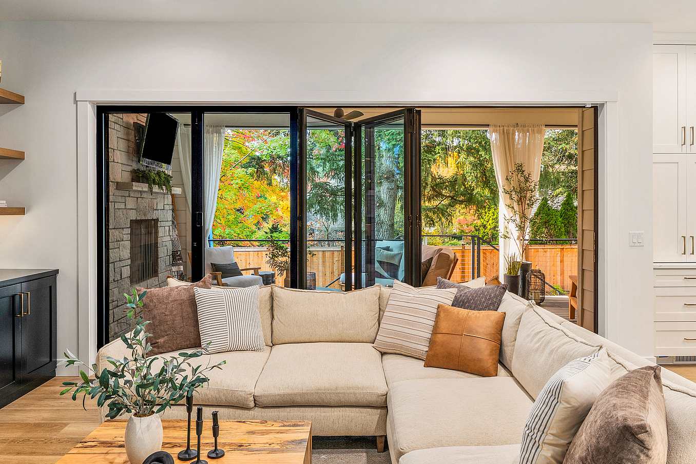 A cozy living room features large bifold glass doors open to an outdoor patio with greenery and seating, inviting natural light to flood the space.