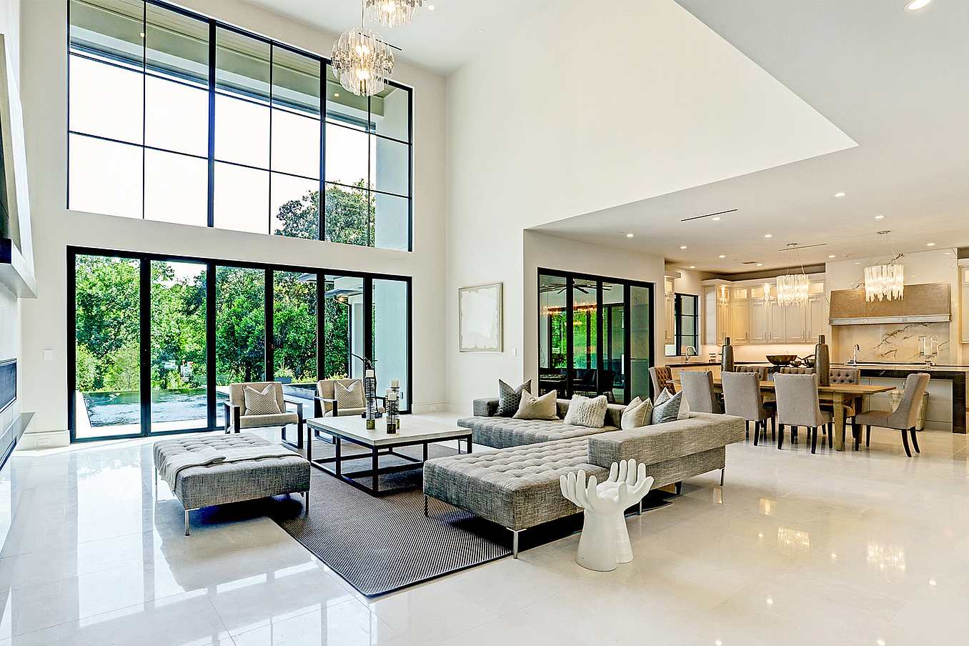 Modern open-concept living room with tall windows and bifold living room doors offering a seamless view into the dining area and kitchen with white cabinetry.
