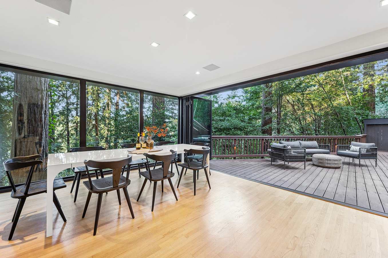 Patio glass doors in a modern dining area opening to a deck with seating and trees.