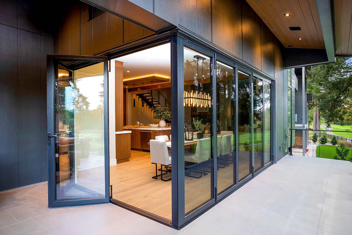 Exterior view of dining room with corner bifold glass system partially open, creating a visual connection to the patio and golf course