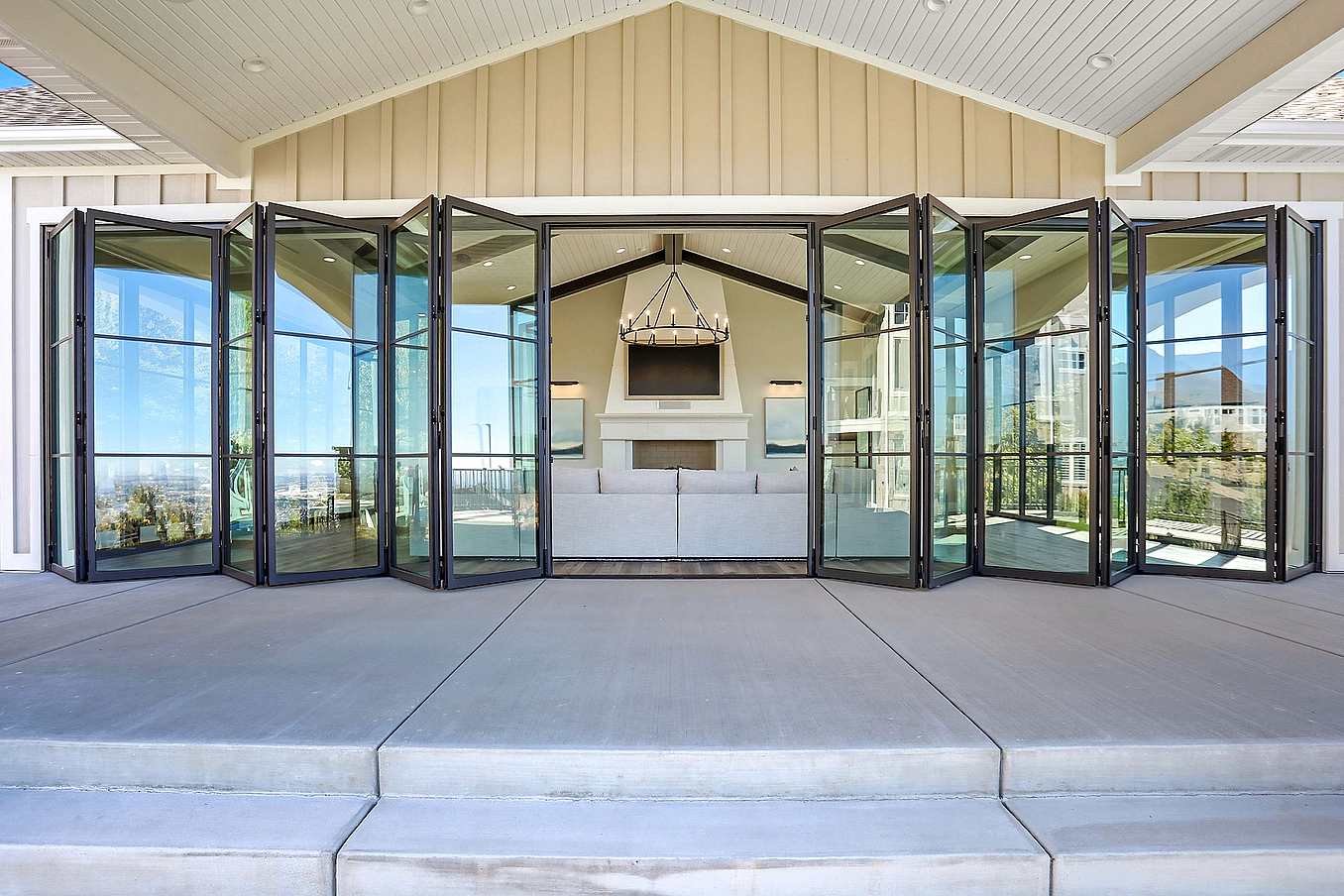 Exterior white pavilion with bifold glass doors partially folded back, revealing patio seating and blending indoor-outdoor living with clean architecture