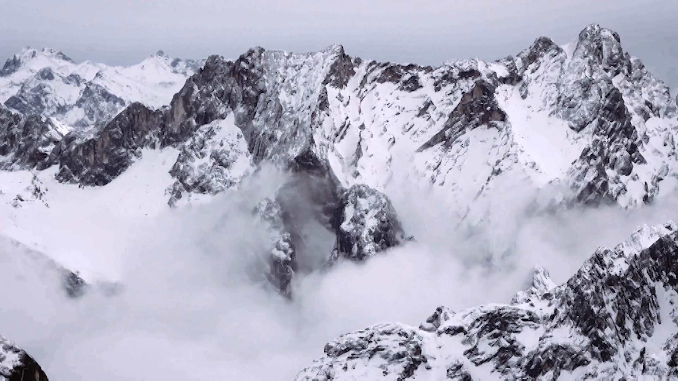 Snow-covered mountain peaks with mist drifting through rocky crevices under a cloudy sky, video vignette featuring high weather performance glass doors.