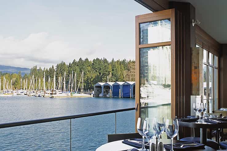 Restaurant dining area with set tables overlooks  a marina with botas through large wood framed accordion glass doors. 