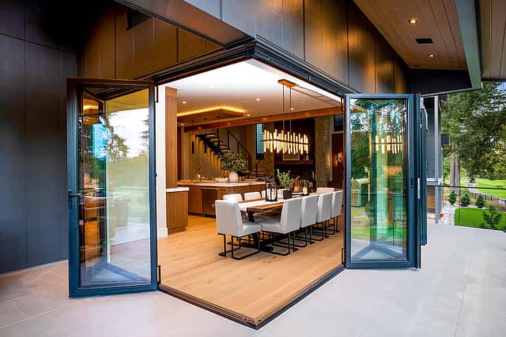 Exterior view of dining room with fully open corner bifold glass doors, seamlessly merging indoor space with patio and golf course views