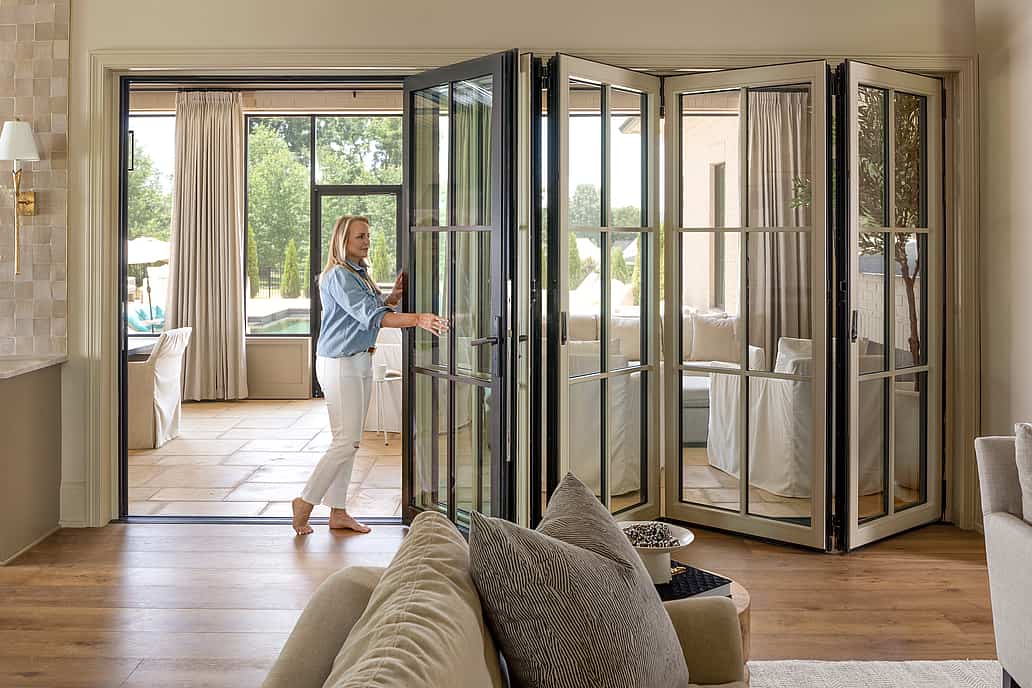 A woman opening bifold glass doors in a living room