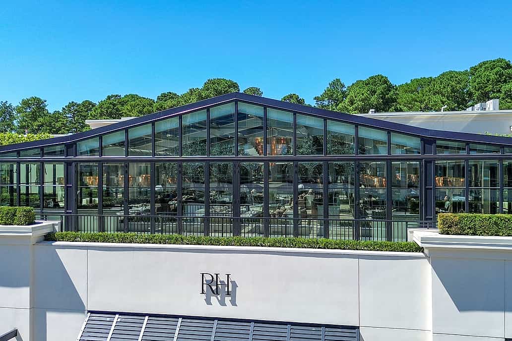 Restoration Hardware rooftop restaurant in Raleigh NC featuring NanaWall SL70 bifold glass doors on a modern glass-walled building with a peaked roof surrounded by greenery under a clear blue sky