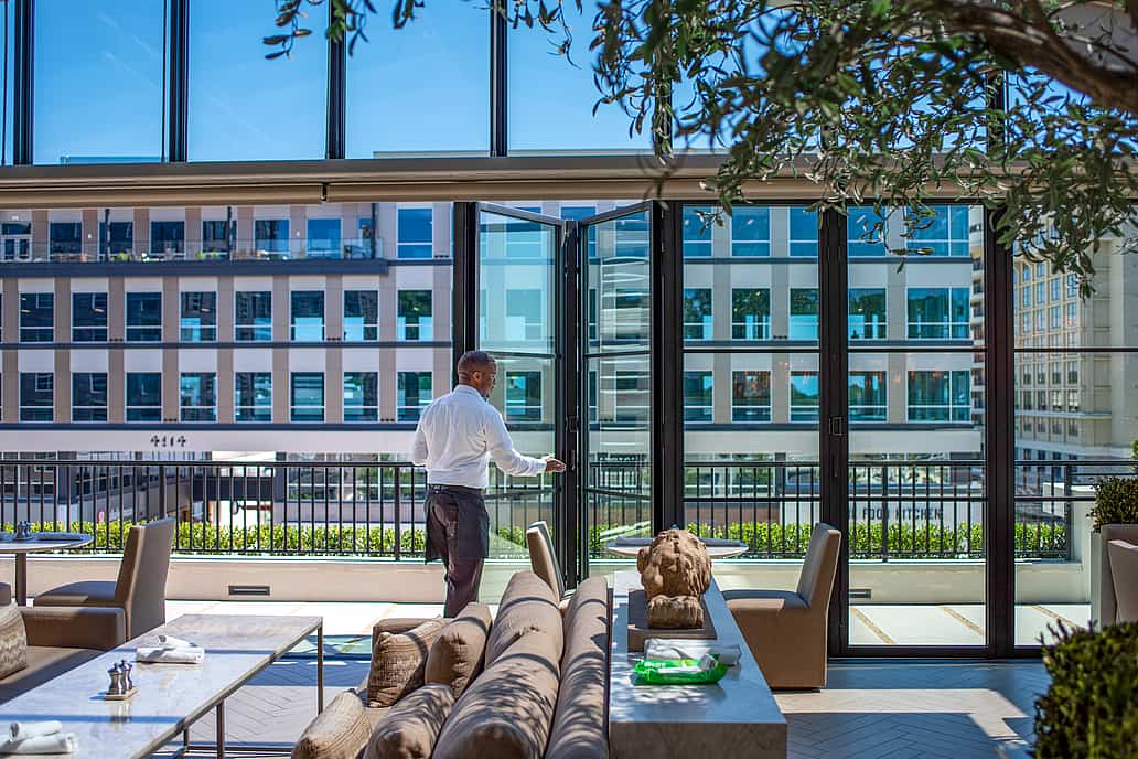 Restoration Hardware rooftop restaurant in Raleigh NC featuring a server standing beside open NanaWall SL70 bifold glass doors with city skyline visible through the windows
