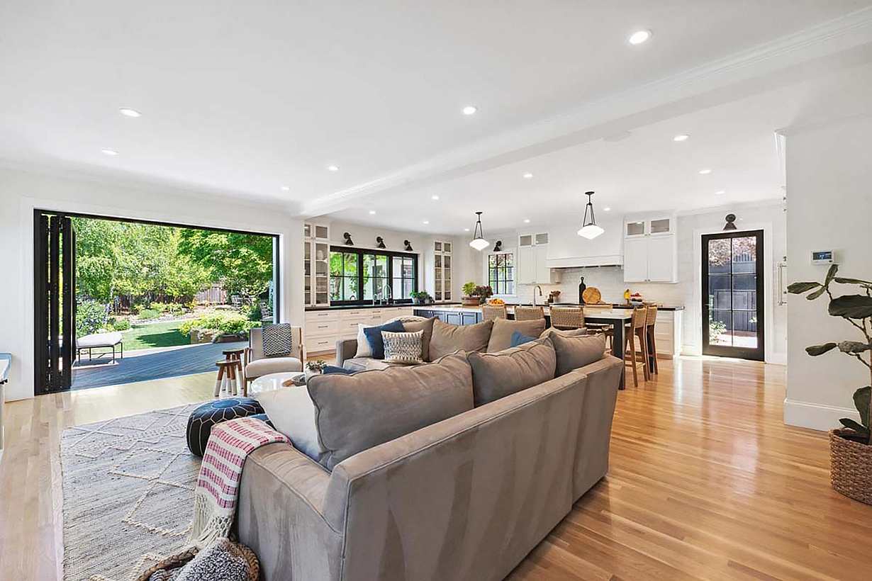 Spacious open-plan living area leading to large folding glass walls that open to a lush garden, offering seamless indoor-outdoor living.