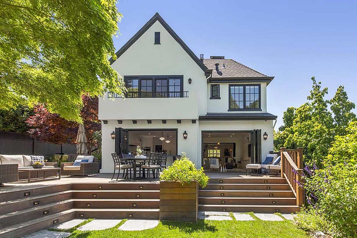 A beautifully remodeled two-story American Craftsman house featuring a gabled roof, large folding glass doors, and an outdoor deck with seating.