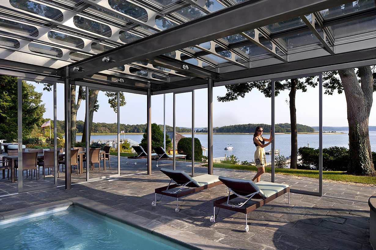 Modern outdoor patio with pool. A women is adjusting the sliding glass door, demonstrating how large openings are possible with unlimited spans of individual panels for an unobstructed view.