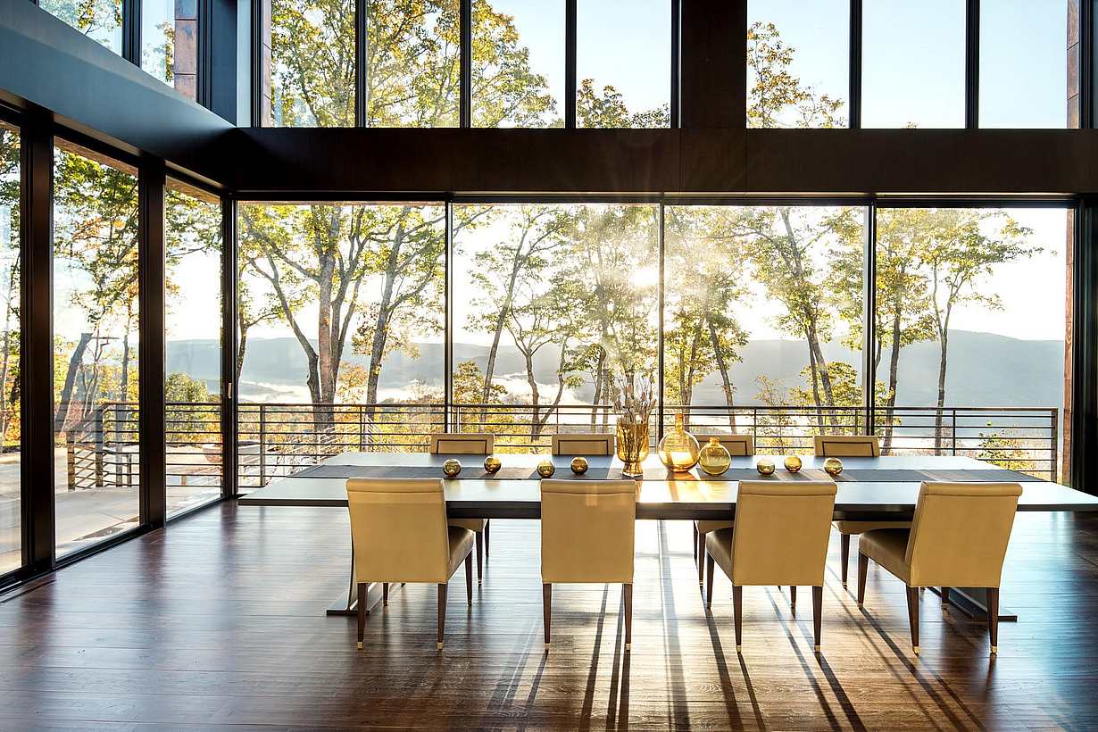 Contemporary dining room with panoramic glass doors opening to scenic mountain view.