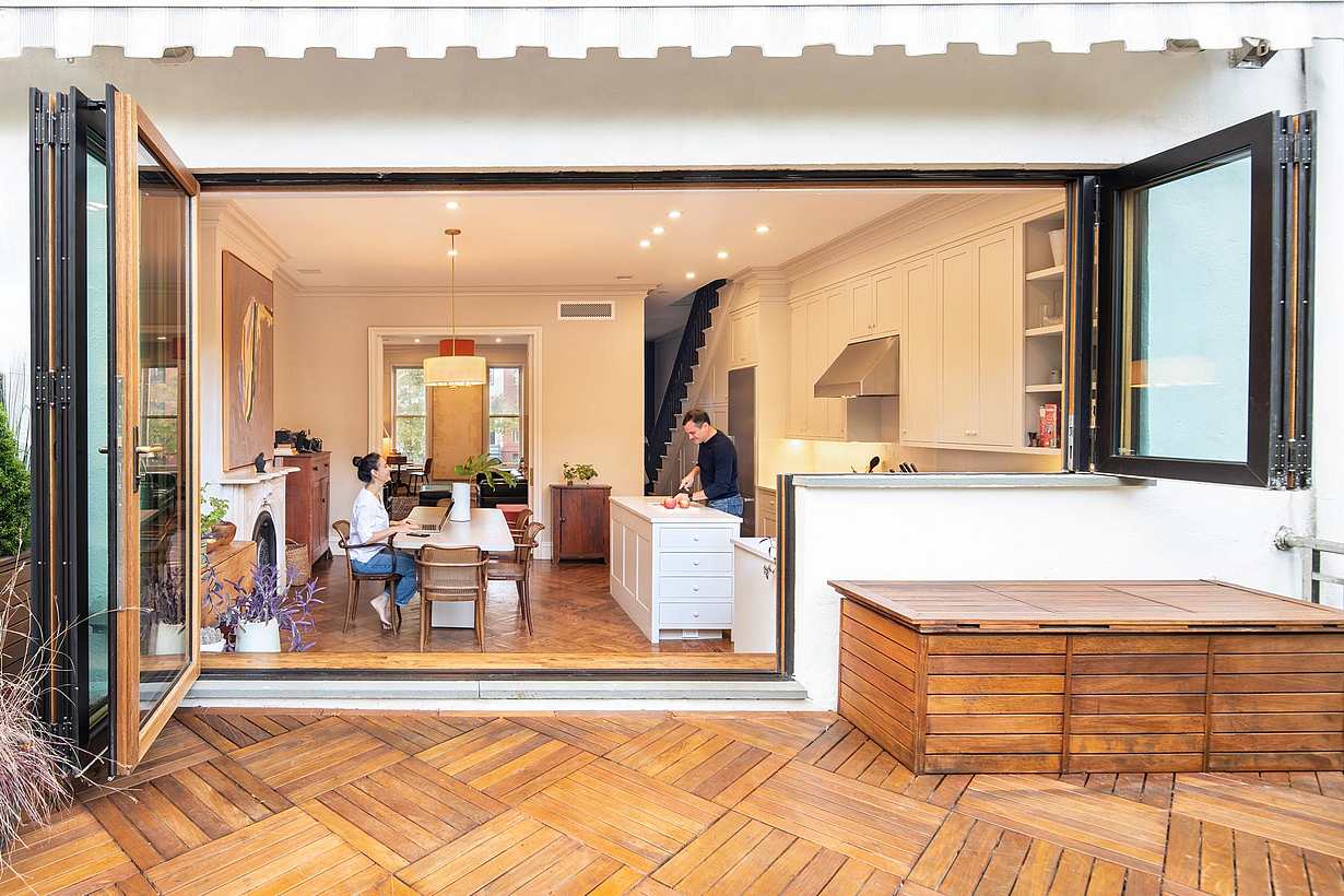 Modern kitchen and dining area with wood-clad folding glass doors that open to a stylish outdoor patio for seamless indoor-outdoor living.