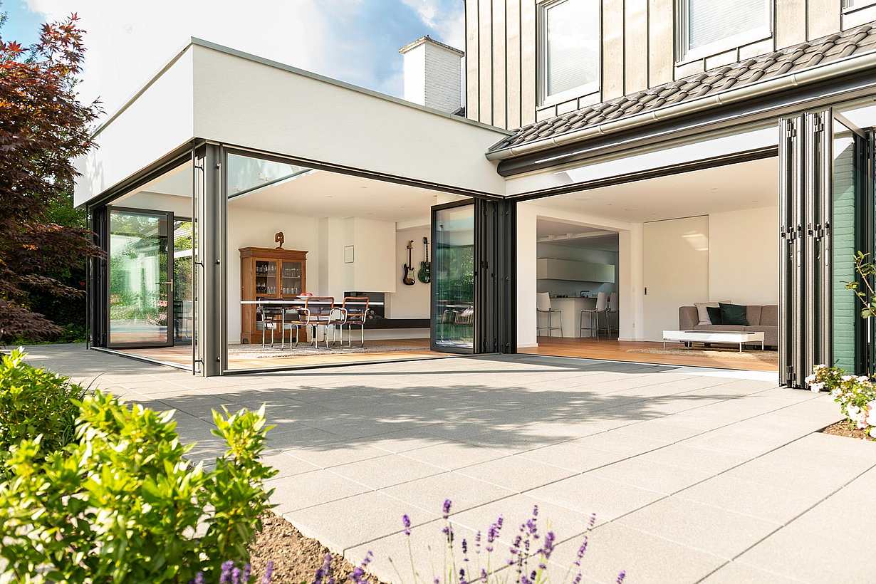 Modern home with large folding glass doors opening to a spacious outdoor patio, seamlessly connecting to an open-concept dining area and living room.