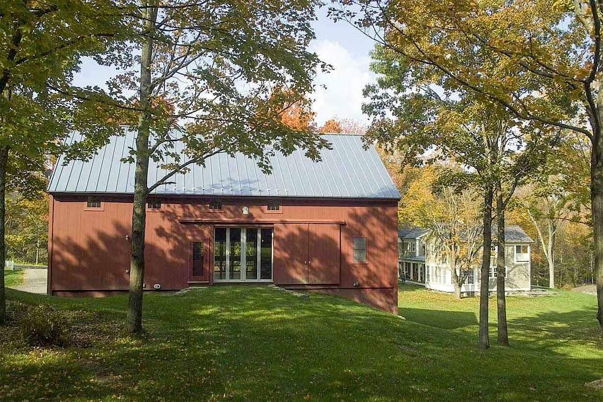 Converted red barn with modern patio doors opening to a green landscape and nearby farmhouse