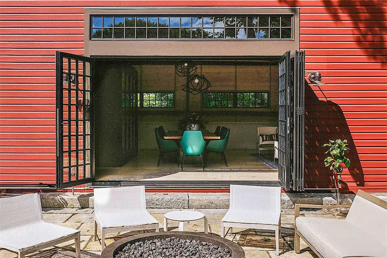 Red barn conversion with bifolding patio doors opening from interior dining space to a modern outdoor patio seating area