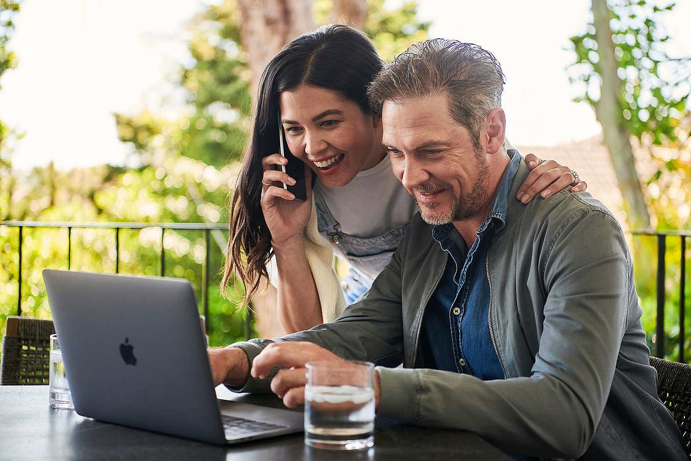 A woman and man sit outside with a laptop, seamlessly connecting with NanaWall glass doors Experts. 