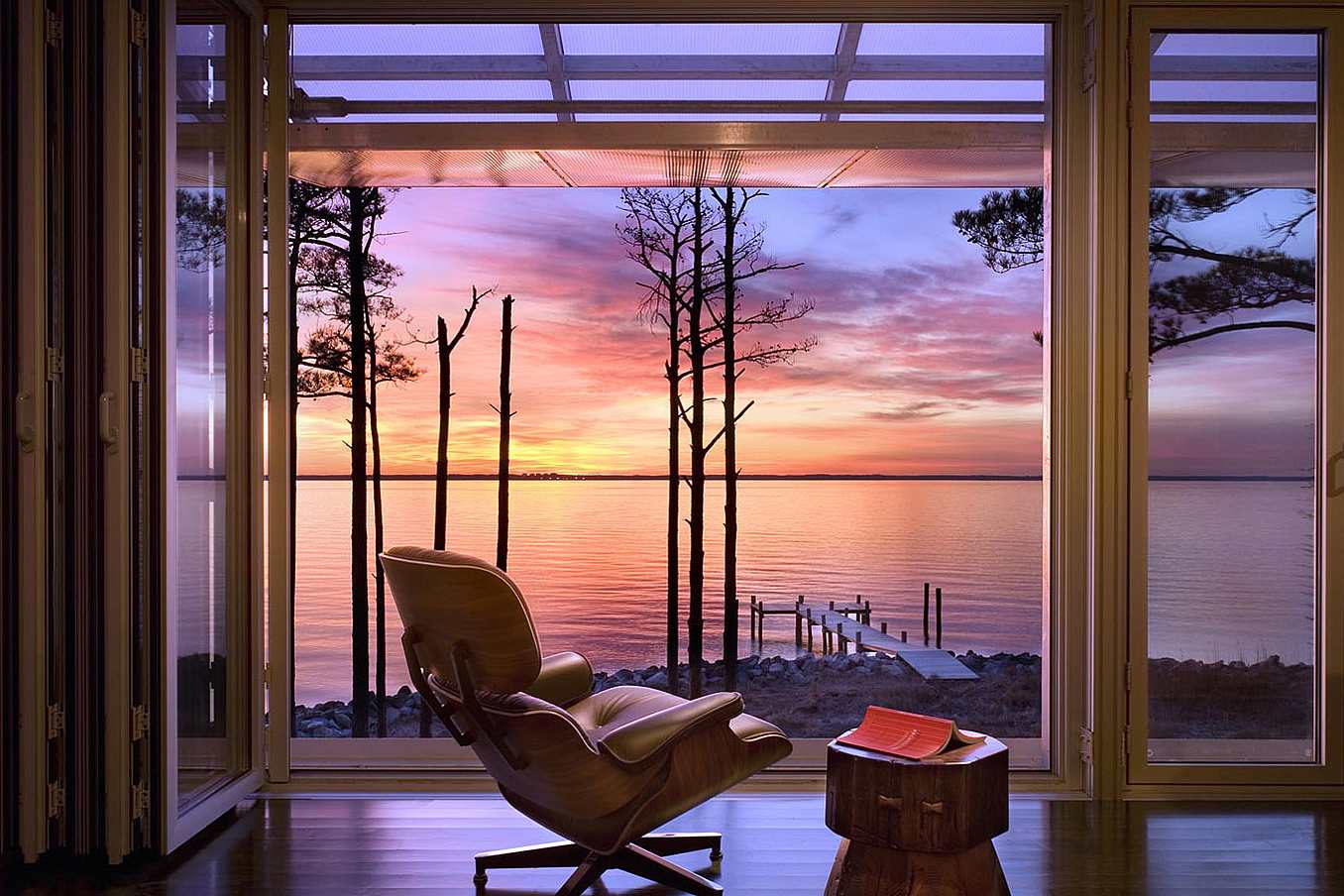 Modern living room with large glass doors opening to a lakeside view at sunset.