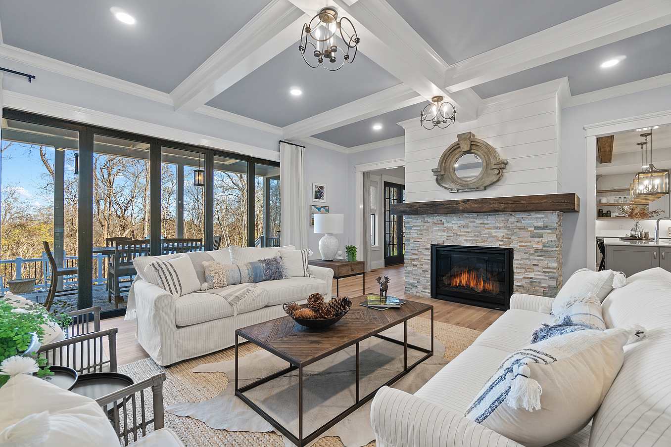 Modern Living room features white walls, a beamed ceiling, modern light fixtures, and folding glass doors that seamlessly connect indoor comfort with the natural beauty outside.