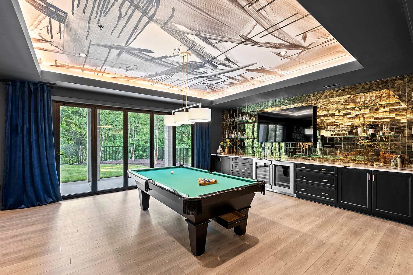 A modern game room with a pool table, black cabinetry, and floor-to-ceiling folding glass doors.