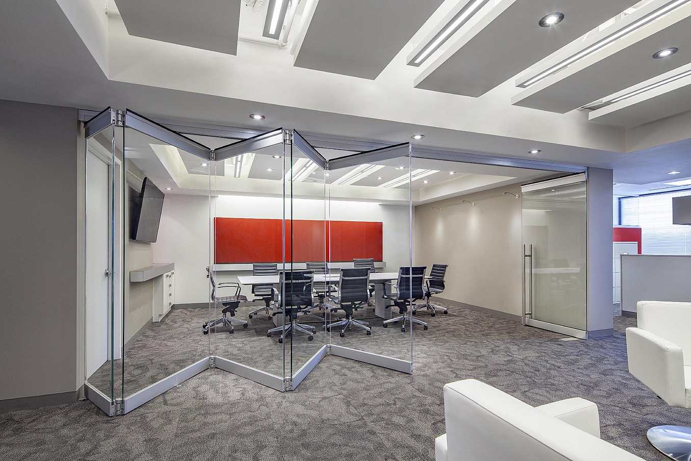 Modern office with frameless folding glass door partitions dividing the workspace from the conference room.