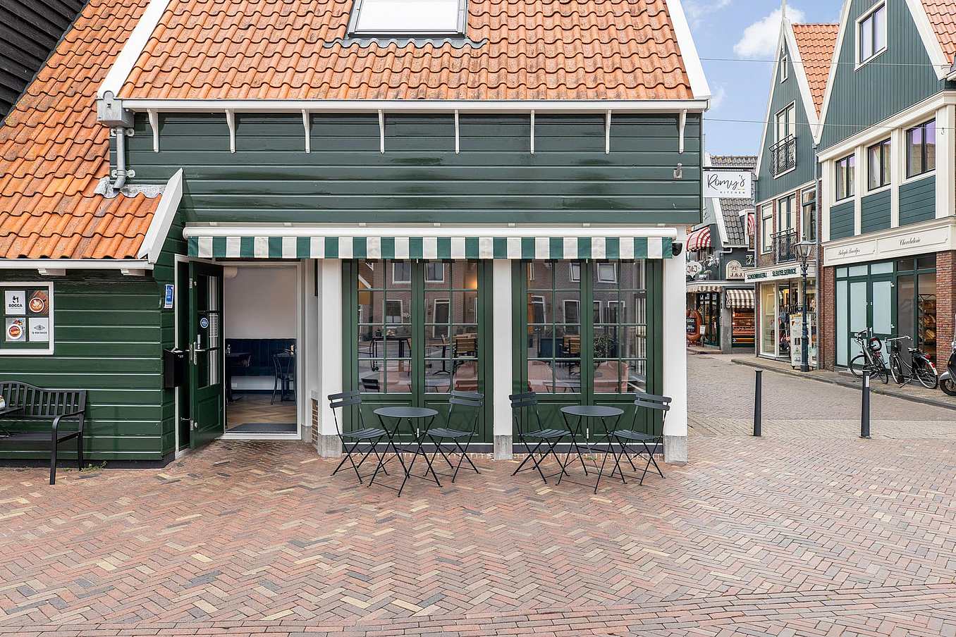 A coffee shop with divided lites wood framed glass walls leading to tables and chairs on a brick street.