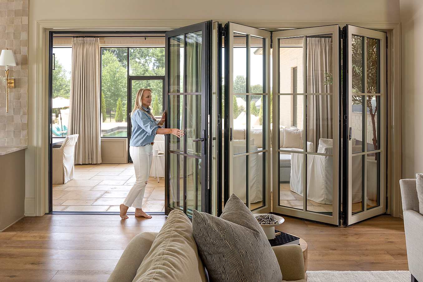 A woman opening bifold glass doors in a living room
