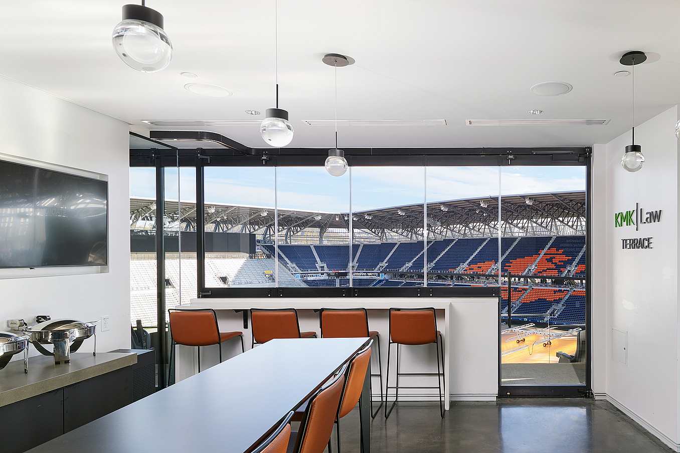 Modern stadium suite featuring commercial sliding windows with integrated swing door, bar seating overlooking the field, and 'KMK Law Terrace'—ideal for VIP and corporate events.